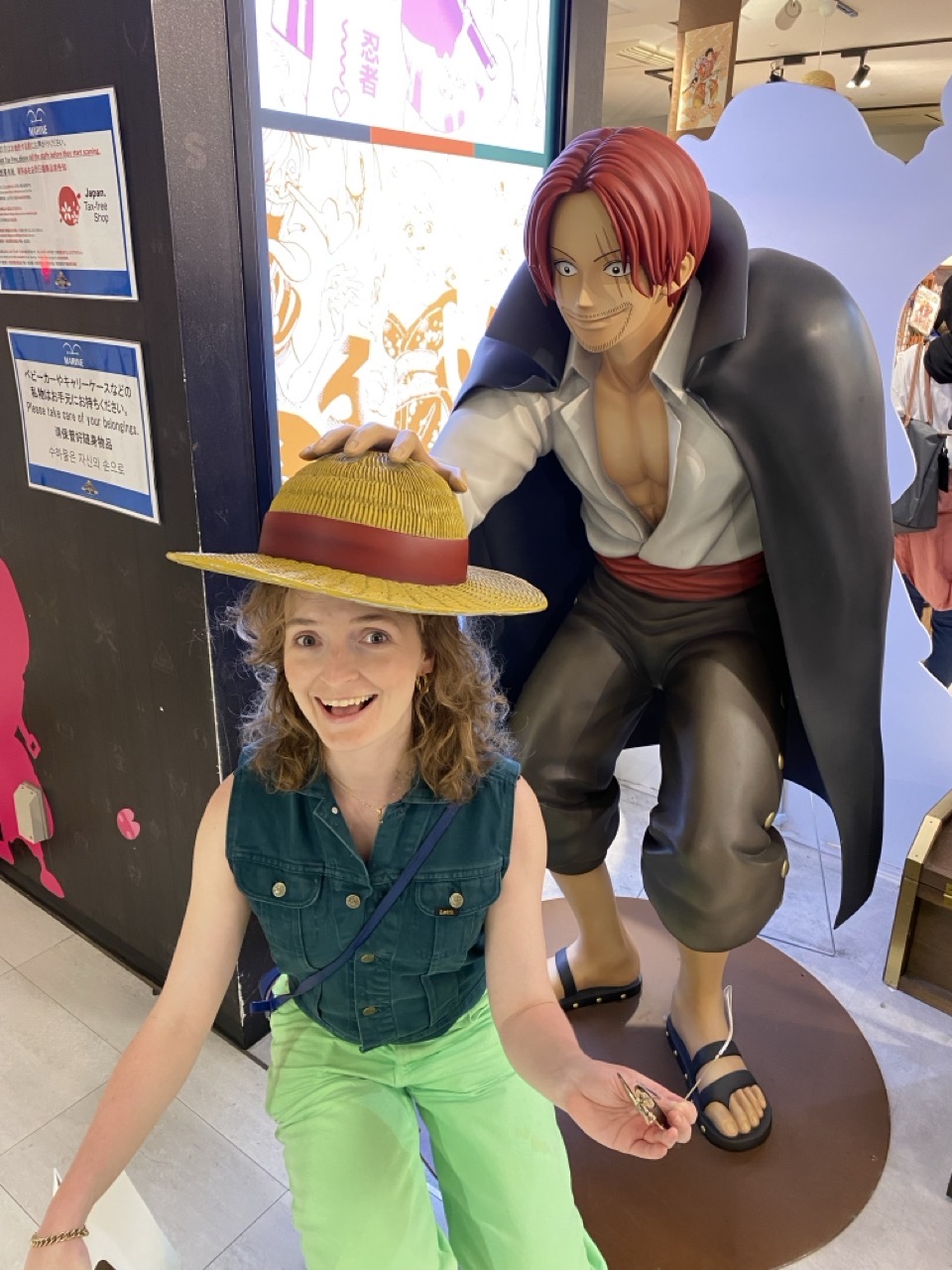 Lucy crouching under a state of a One Piece character putting a straw hat on her head