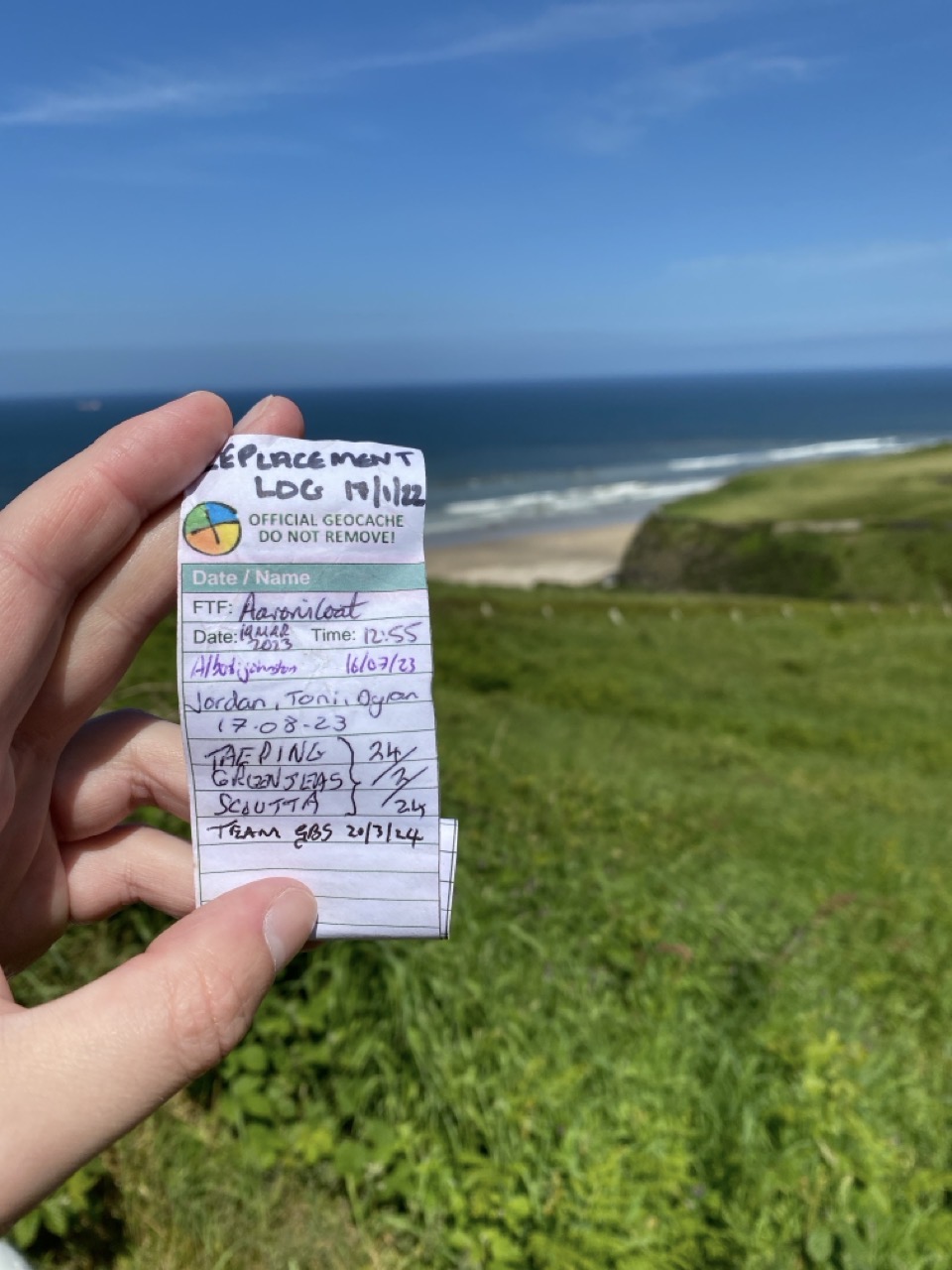 The log book from the geocache, with blue sky and sea in the background.