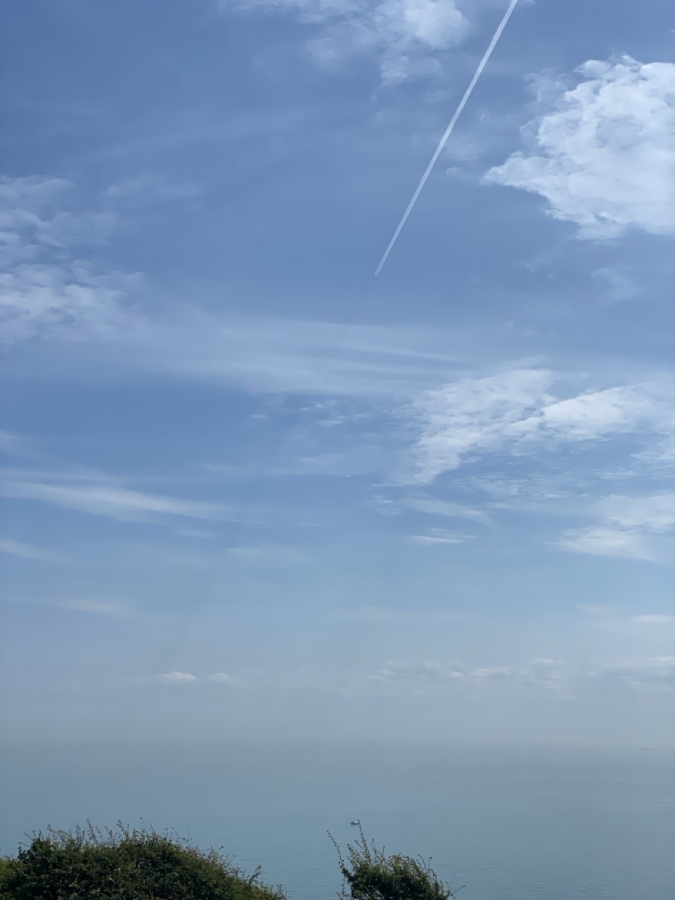A blue sky over the sea with a jet contrail and a shadow extending from it towards the horizon.