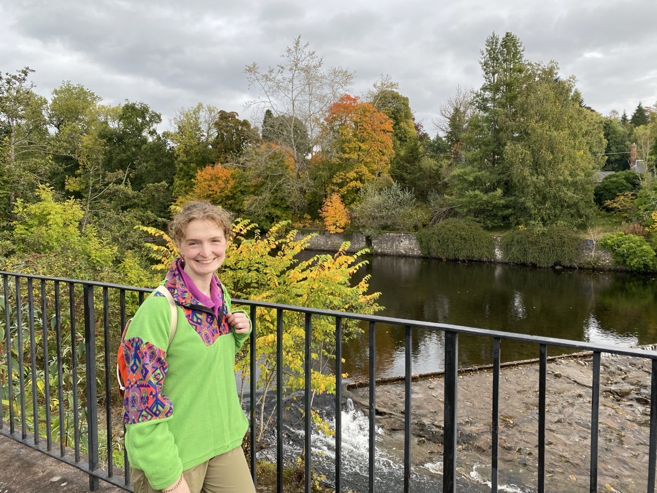 Lucy by the river. There are autumn coloured trees in the background.