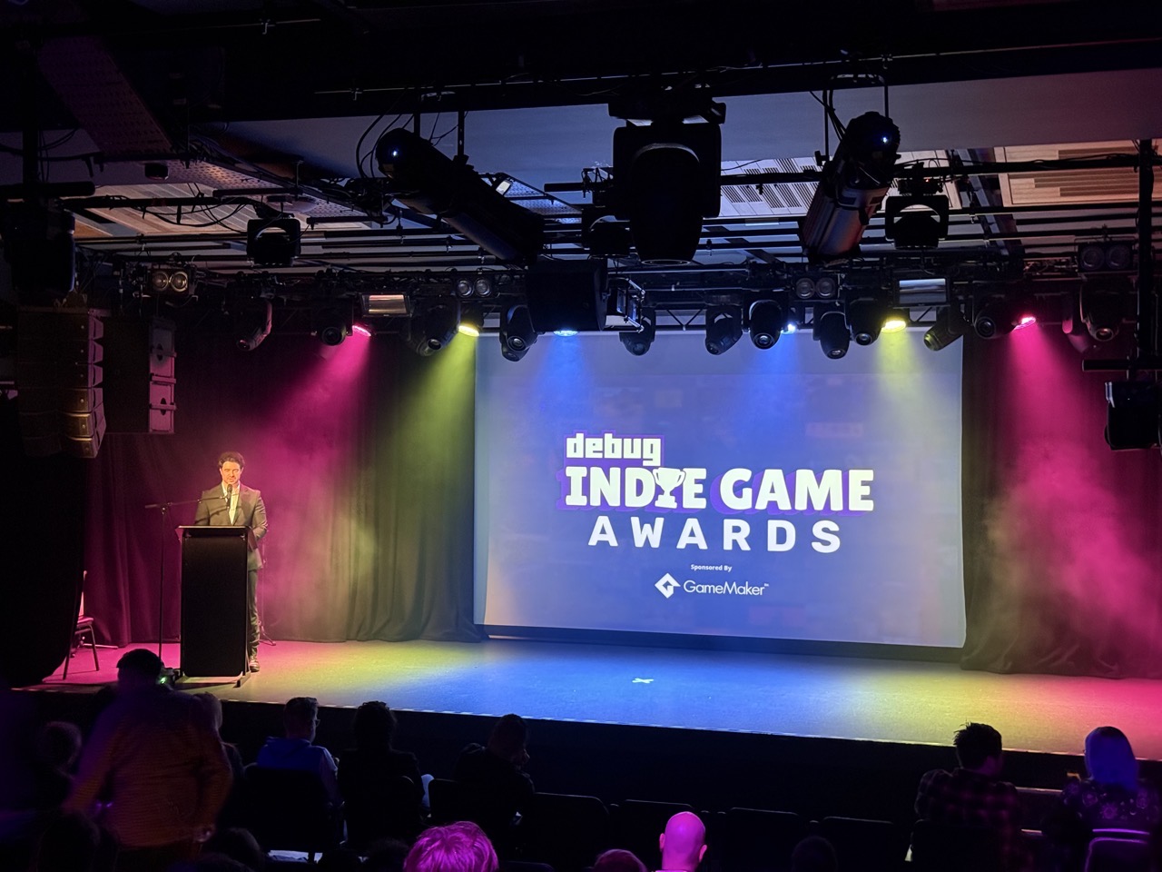 The stage at the indie game awards. The host is off to the left and there is blue and green and pink lighting